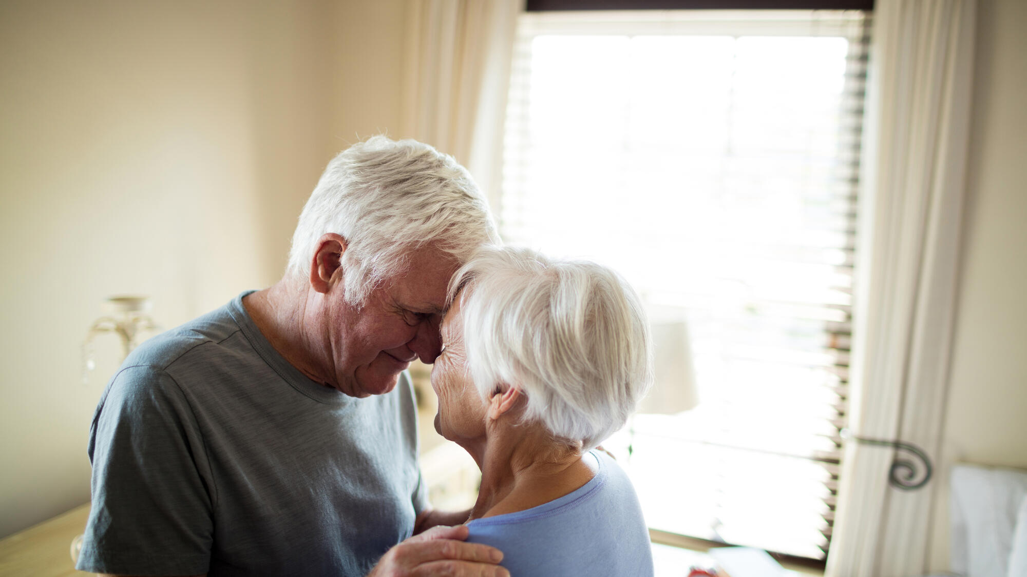A senior couple holding one another by a window