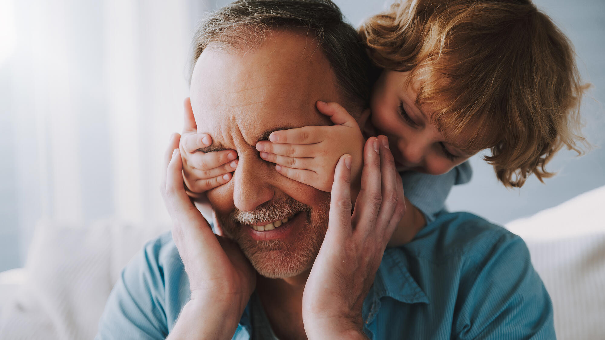 A child covering their grandfather's eyes, playfully.